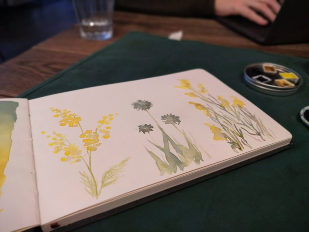 Focus sur un carnet d'aquarelle ouvert sur quelques illustrations de fleurs
jaunes et bleues.
