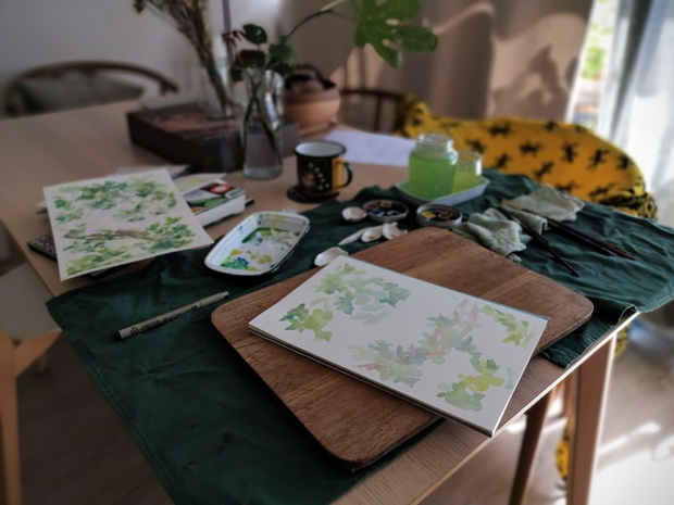 Une table de travail avec des illustrations à l'aquarelle. Les illustrations
représentent des branchages et des feuilles vertes.
