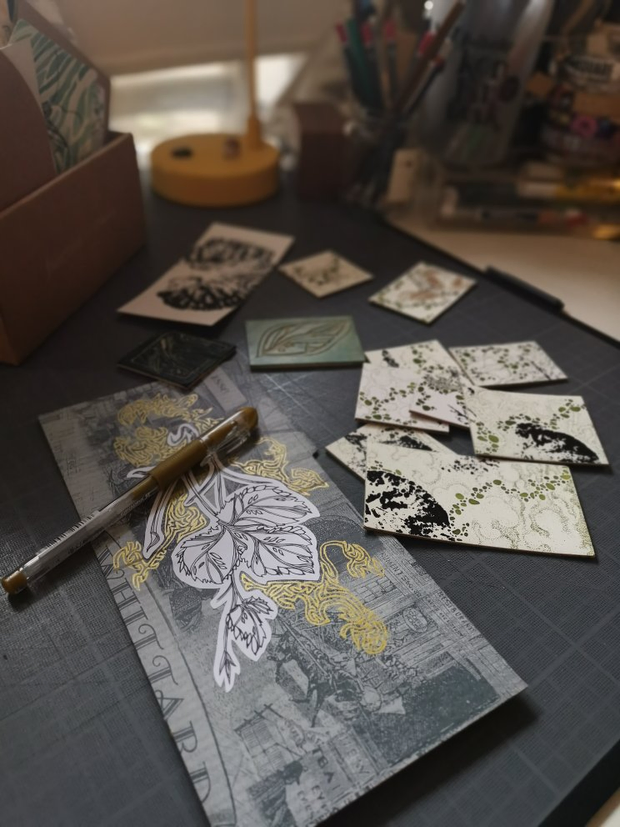 Des mini-illustrations à l'encre étalée sur un bureau. Les illustrations
représentent des motifs végétaux un peu abtraits à l'encre noire et
à l'encre verte.
