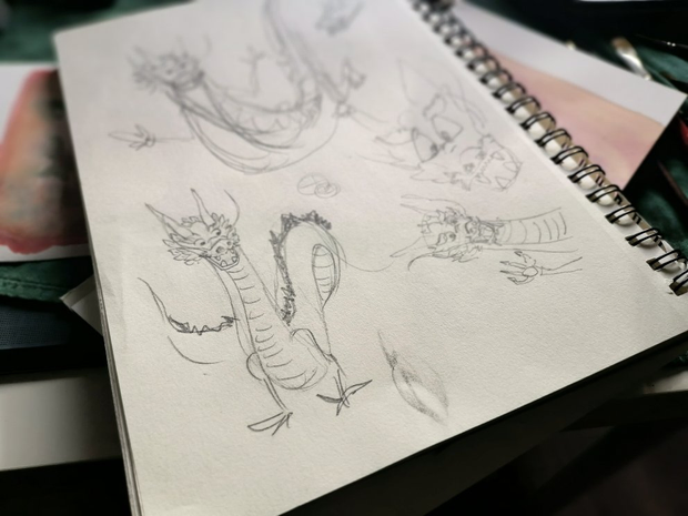 Des croquis de dragon faits au crayon à papier sur un carnet.
